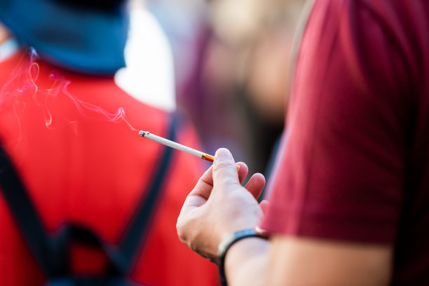 特写男子身穿红色衬衫，手里拿着细长的香烟，白天在意大利罗马街头吸烟，不健康图片下载