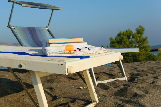 甲板上的椅子与书籍和夏天的帽子在海滩上对抗清澈的蓝色天空图片下载