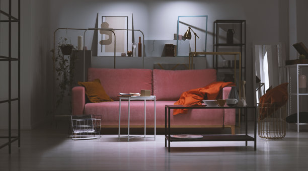 夜景粉粉色沙发，橙色枕头和毯子，在艺术收藏家的公寓充满金属架子和抽象画，真实的照片图片下载