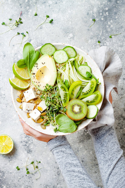 女孩拿着素食排毒佛碗，里面有奎奴亚藜，鳄梨，西葫芦面条，黄瓜，番茄，酸橙，猕猴桃，豆腐，菠菜，微绿色蔬菜，披萨。图片下载