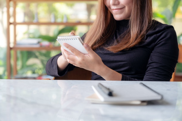 一个美丽的商业女人的特写图片，拿着笔记本在咖啡馆与绿色自然的背景图片下载