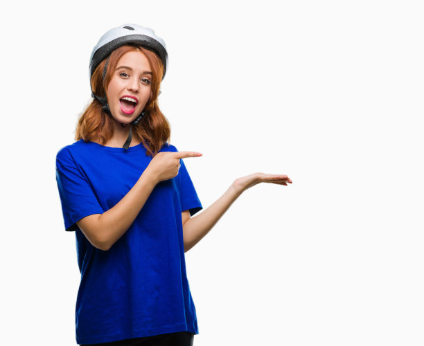 年轻美丽的女人戴着自行车头盔在孤立的背景惊讶和微笑的相机，同时提出与手指。图片下载