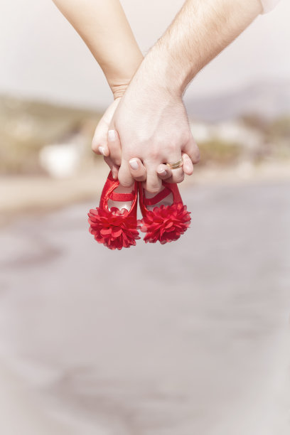 日落时分，一对怀孕的夫妇手牵着手，穿着红色婴儿鞋图片下载