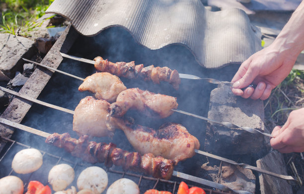 男人手里拿着烤蔬菜、鸡肉和猪肉在明火上。烤架上放洋葱，蘑菇，番茄和红辣椒。砖做的烧烤场所。夏日美食照片图片下载