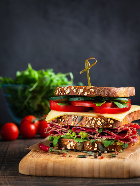 特写美味的三明治与意大利腊肠，奶酪和新鲜蔬菜在乡村木砧板在木桌上，选择性的焦点。空间的文本。垂直的。俱乐部三明治的概念。图片下载