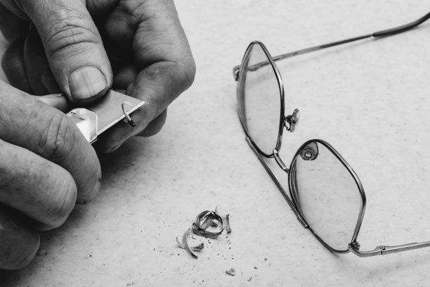 桌子组成与眼镜，铅笔刨花和手的老人谁削铅笔与刀在灰度。单色背景。图片下载