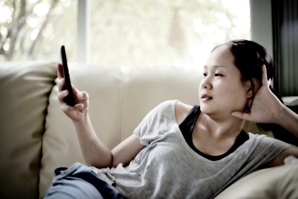 特写年轻女子放松在沙发上与她的智能手机:柔和的焦点图片下载