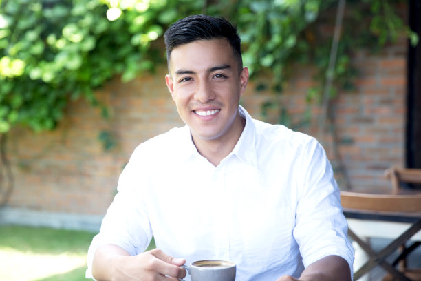 一个年轻的拉丁男子在街上的咖啡馆喝咖啡。图片下载