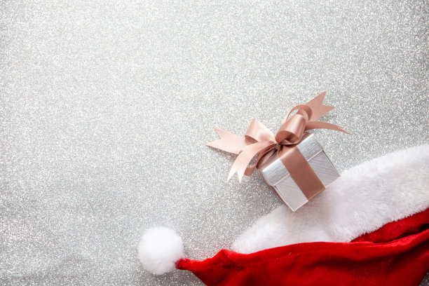 一顶圣诞老人帽和一个银光背景上的小礼盒图片下载
