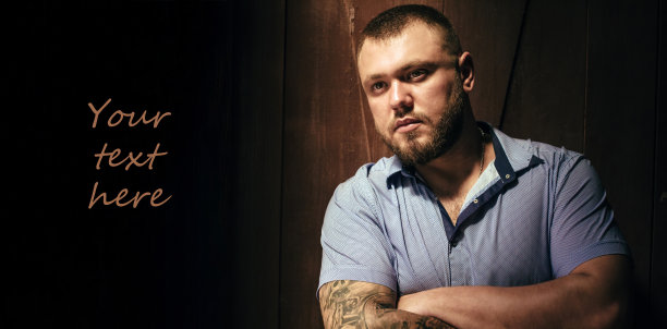 复制空间，你的文本在这里，一个手臂上有纹身的凶残的大胡子男人，一个在棕色木墙的戏剧性光线下的男人的肖像，一个手臂上有纹身穿着衬衫的迷人的大胡子男人图片下载