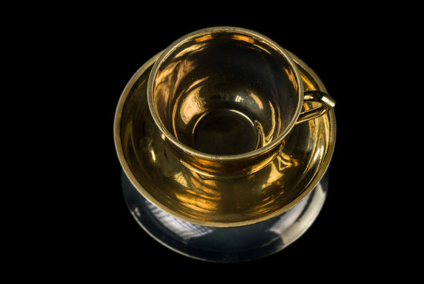 镀金茶杯放在一个碟上，孤立在黑色的背景上图片下载