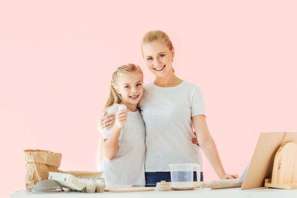 年轻快乐的妈妈和女儿看着镜头，女孩抱着鸡蛋孤立在粉红色的鸡蛋上图片下载