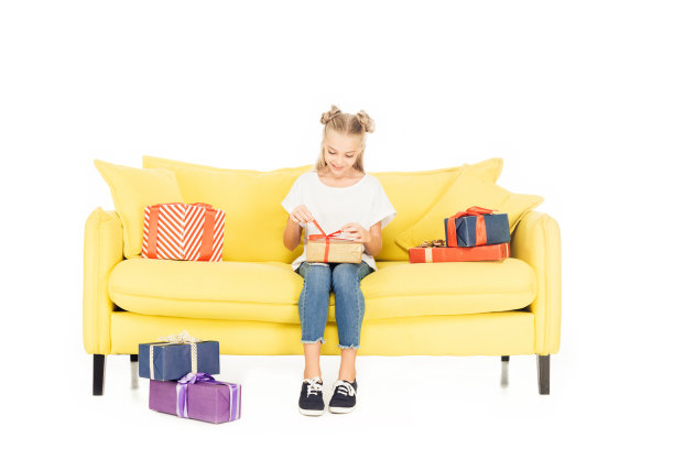 微笑可爱的孩子打开礼物在黄色的沙发上孤立的白色图片下载