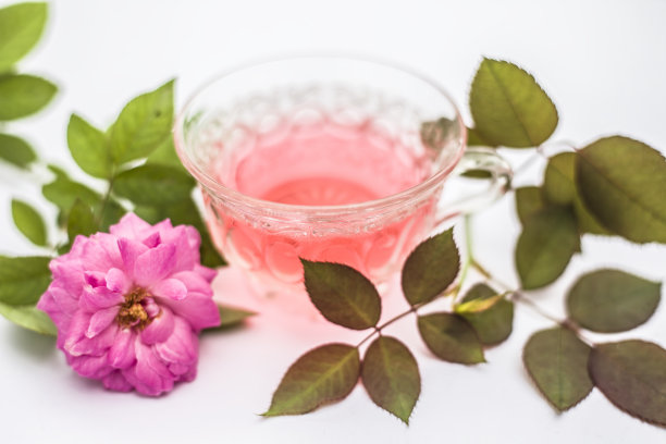 近距离观察玫瑰茶的粉红色与蔷薇花瓣孤立在枯萎在透明杯。图片下载