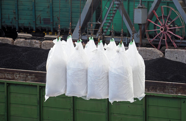 工业港口的散货船上正在装白色的袋子。装袋起重机上的货物。火车车厢装载，铁路装载图片下载