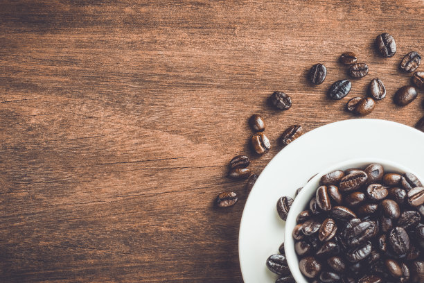 用白色陶瓷杯和勺子在木桌上烘焙咖啡豆。咖啡中的咖啡因适量可以帮助减少烦躁。抑郁的情绪包括压力。图片下载