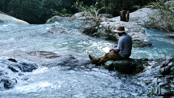 年轻人使用笔记本电脑在瀑布和露营。旅行和自由职业的工作理念图片下载