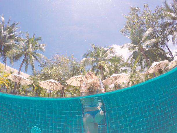 水下拍摄的女性在游泳池的梯子上观看棕榈树以上;年轻女子在游泳池度假图片下载