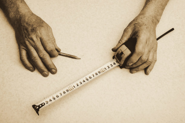 老年工人的手与铅笔和轮盘紧靠在深褐色的色调。单色背景。图片下载