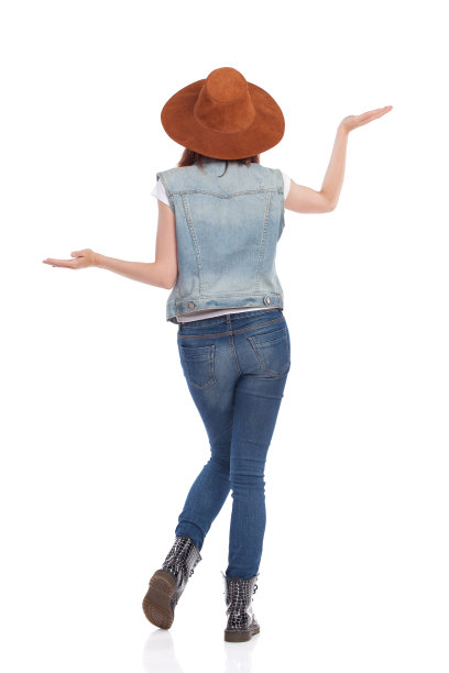后视图的年轻女人在牛仔裤，靴子和绒面革帽子与手举起图片下载