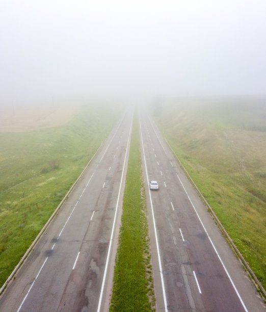 鸟瞰图的道路与一辆经过的汽车和田野在秋天，雾蒙蒙的早晨。无人机拍摄的照片图片下载
