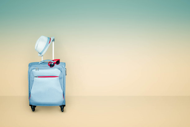 浅蓝色行李箱，浅米色和蓝色背景，搭配夏日帽和时尚太阳镜，夏日度假旅游理念，自由空间，有抄袭的地方。图片下载