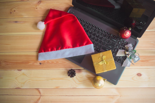 有笔记本电脑、圣诞老人帽和圣诞装饰品的圣诞工作区。图片下载