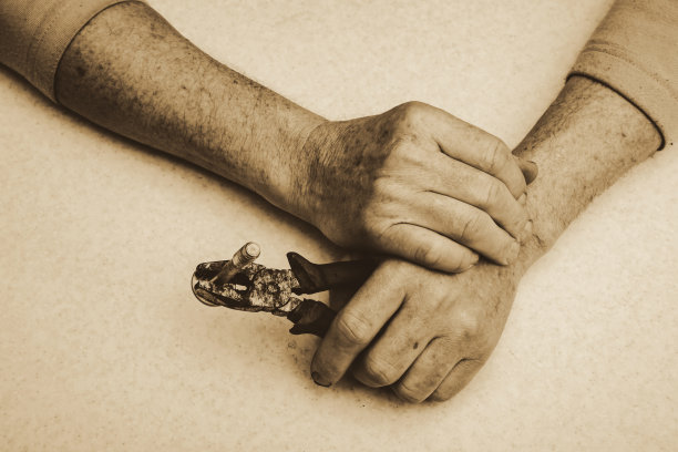 老工人手里拿着大螺栓钳子，以深褐色的音调靠近。单色背景。图片下载