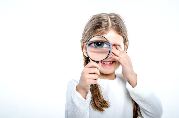 一个小女孩的肖像，手里拿着一个放大镜。女孩用手合上左眼，用右眼透过放大镜看。图片下载