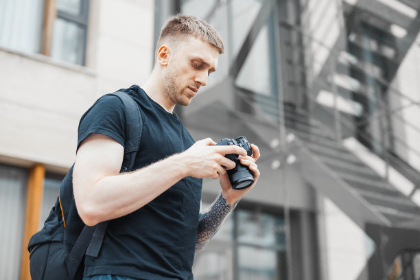有魅力的男人站在楼梯旁，在看相机里的照片。图片下载