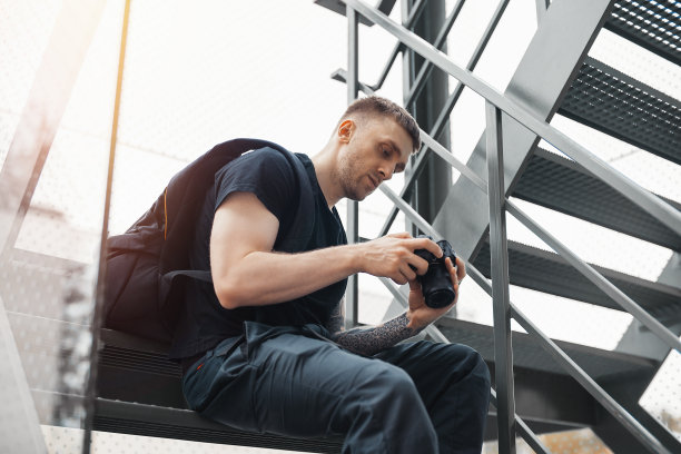 有魅力的男人坐在楼梯前，在看相机里的照片。图片下载