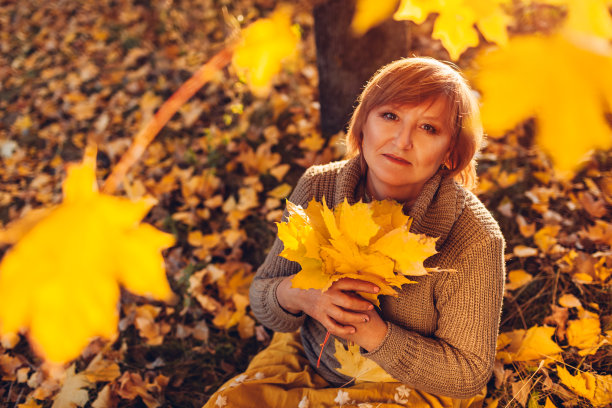 中年妇女捧着一束枫叶。女士欣赏秋色，放松心情图片下载