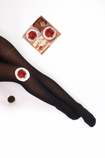 创意照片的女性腿在黑色连裤袜与一杯咖啡和一盒小蛋糕在白色的背景。的概念。图片下载