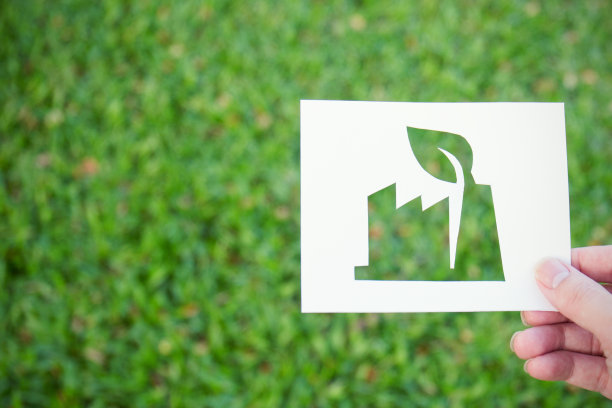 手握剪纸与工厂形状的标志在绿色玻璃背景。标志和标志背景旗帜的地球日概念图片下载