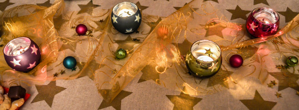圣诞餐桌装饰用球形彩色眼镜蜡烛，一个桌布与金色的星星和小彩色圣诞球在烛光。图片下载