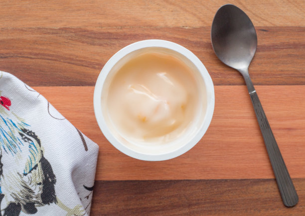 酸奶在塑料杯近距离与小银勺，俯视图照片的桃子酸奶在木制桌子的背景图片下载