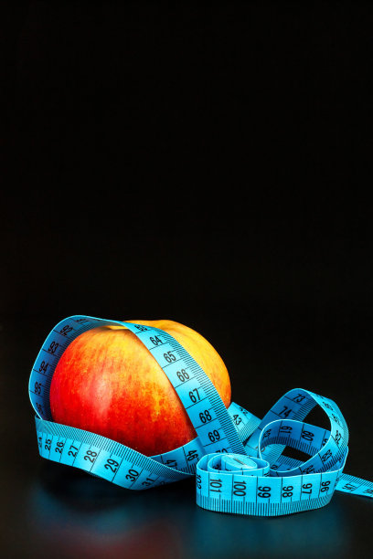 红苹果。黑色背景上，用裁缝卷尺包着的红苹果。减肥的概念。健康的饮食习惯。图片下载