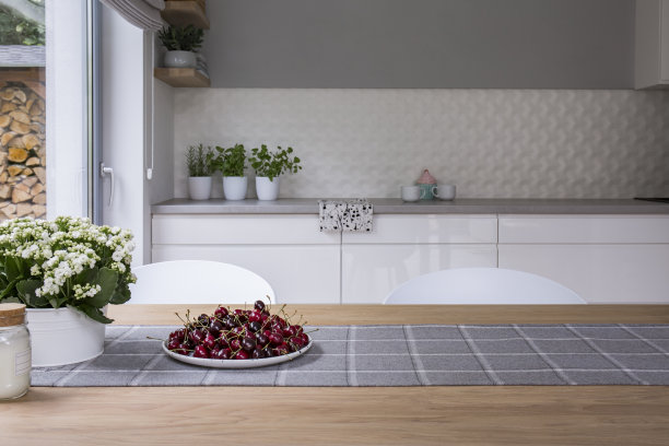 白色和灰色的厨房内部有窗户，木制餐桌上放着樱桃和鲜花。真实的照片图片下载