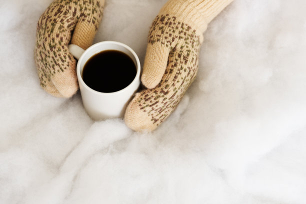 手上戴着蓝绿色手套的女人正拿着一个装着热咖啡或可可的杯子。图片下载