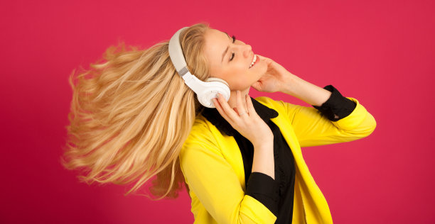 美丽的年轻女子在黑色和黄色充满活力的裙子跳舞，她听着音乐在粉红色的背景图片下载