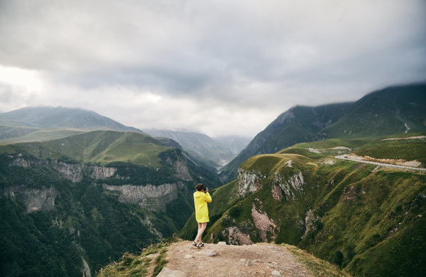 一个穿着黄色雨衣的小女孩拍摄着群山。格鲁吉亚。夏天。8月。女孩正在拍摄山的照片。图片下载