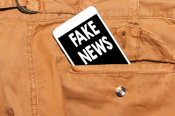 写便条显示假新闻动机召唤。商业照片展示虚假的未经证实的信息骗局手机在裤子口袋上的概念图片下载