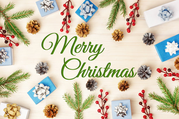 在一个浅色木制背景的中央写着“圣诞快乐”。冷杉枝、球果、红色装饰浆果和礼品盒呈圆圈展开。节日的照片。图片下载