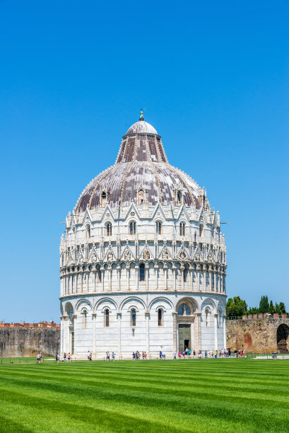 垂直照片与非常著名的巴蒂斯特。这座古老的建筑坐落在大教堂广场上，紧挨着斜塔。前面是绿色的草坪，后面是蓝色的天空。图片下载