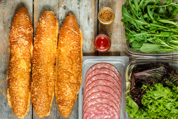 夹有面包卷、生菜、香肠和火腿的三明治，在木制的背景上。野餐的食物。俯视图图片下载