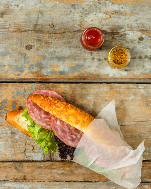 夹有面包卷、生菜、香肠和火腿的三明治，在木制的背景上。野餐的食物。俯视图图片下载