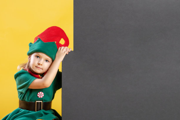 穿着精灵服装的小女孩。在黑色背景的子元素附近有一个用于文本、复制的空间。节日的照片。图片下载