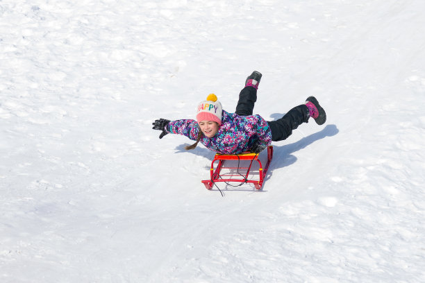 快乐微笑的女孩在雪橇上滑下雪山图片下载