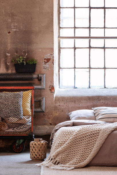 灯笼旁边的床和毯子在明亮的阁楼卧室内部有枕头和窗户。真实的照片图片下载