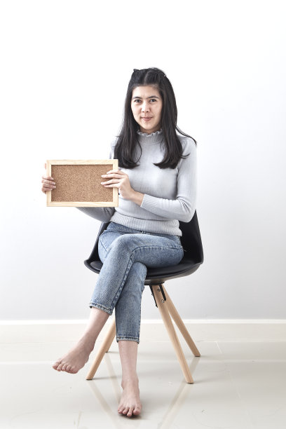 微笑的女人与公告牌勇气姿态姿态坐在椅子上的白色墙壁背景图片下载